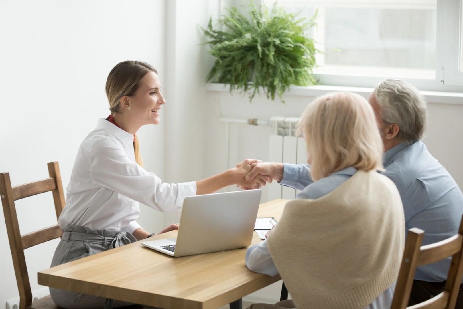 A woman shaking hands with another person over a laptop.