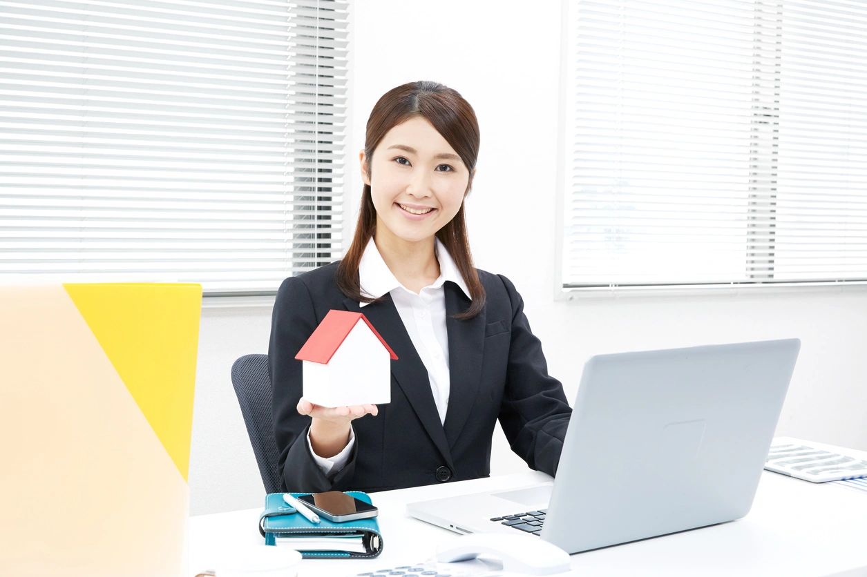 A woman holding a paper house in front of her laptop.